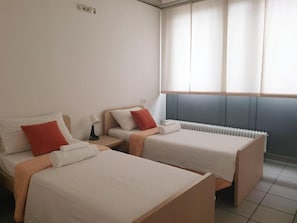 Una habitación de hotel con dos camas individuales, una mesita de noche, una lámpara y una ventana con persianas.