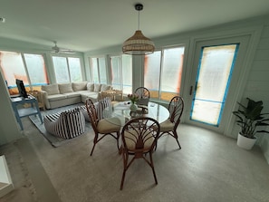 A modern living room with a sectional sofa, a glass dining table, and wicker chairs. - Spoonbill Cottage | 3-Min Walk to Beach | Heated Pool | 4BR Family Retreat (Bradenton Beach)