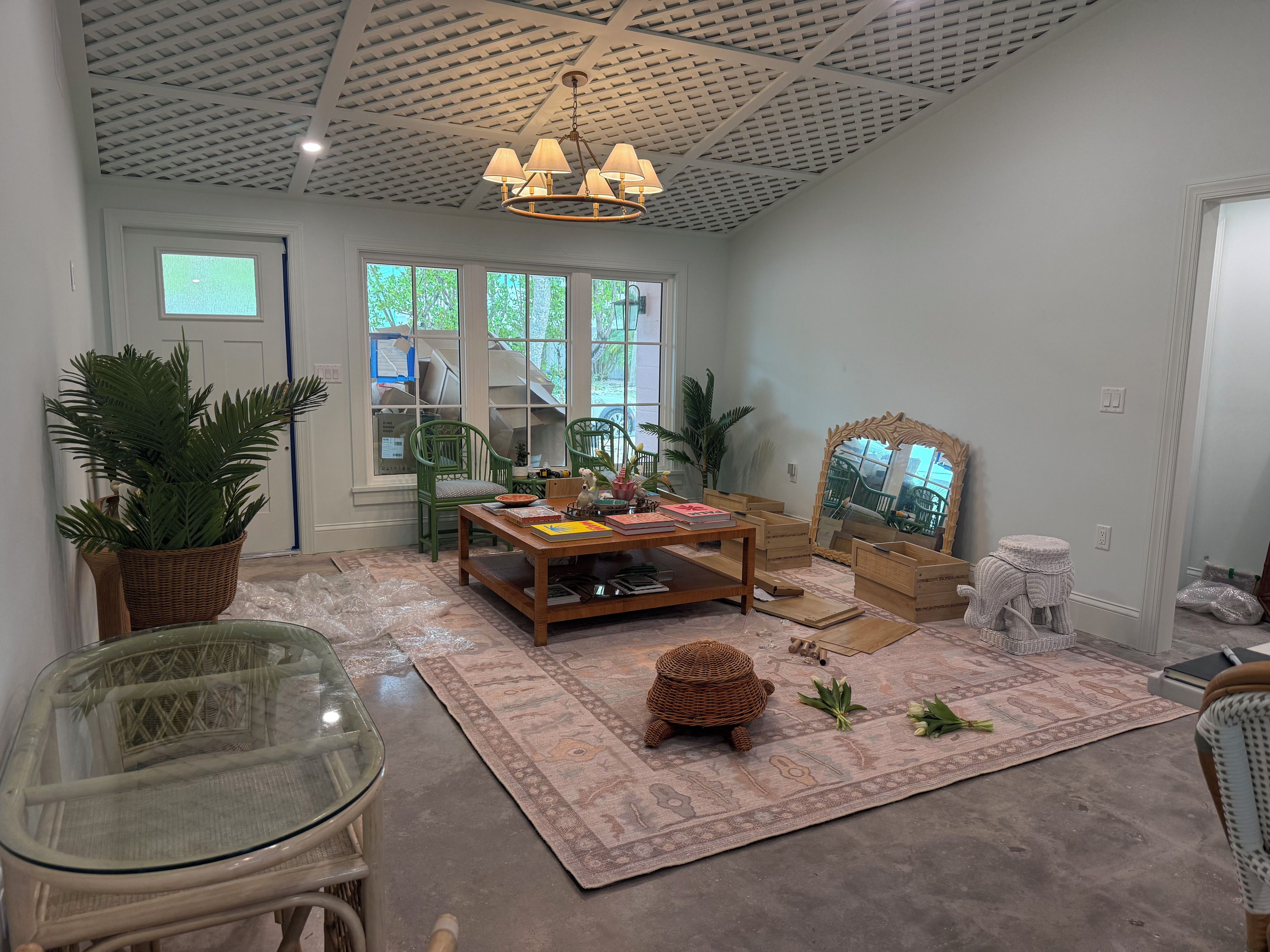 A room with a wooden coffee table, green chairs, a glass table, a woven basket, and a large mirror.