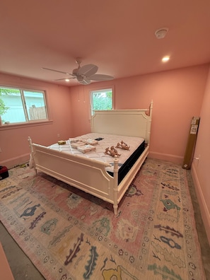 A bedroom with a bed, a ceiling fan, a window, and a patterned rug. - Spoonbill Cottage | 3-Min Walk to Beach | Heated Pool | 4BR Family Retreat (Bradenton Beach)