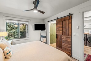 A bedroom with a bed, a television, a sliding barn door, and a view of a laundry area. - Sunrise 304 – Spacious Mountain Retreat Near Steamboat Resort! (Steamboat Springs)