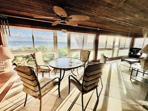 A room with a round table, chairs, a ceiling fan, and large windows offering a view of the beach. - An Island Time | Direct Beachfront | 2BR Upstairs Retreat | Old Florida Charm (Holmes Beach)