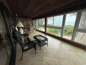 A spacious room with a large window offering a view of the sea, a sofa, a coffee table, and a lamp. - An Island Time | Direct Beachfront | 2BR Upstairs Retreat | Old Florida Charm (Holmes Beach)
