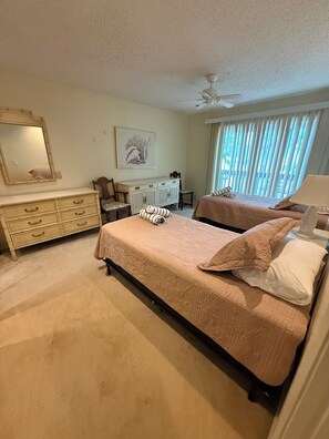 Ein Schlafzimmer mit Bett, Kommode, Spiegel, Deckenventilator und Fenster mit Jalousien.