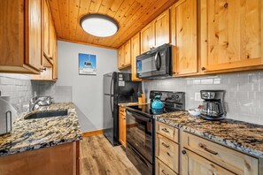 A kitchen with wooden cabinets, a stainless steel refrigerator, a microwave, a stove, and a coffee maker. - Top-floor ski-in/ski-out retreat with stunning gondola views and private balcony (Steamboat Springs)