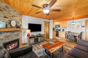 A cozy living room with a fireplace, a television, and a dining area with wooden furniture. - Top-floor ski-in/ski-out retreat with stunning gondola views and private balcony (Steamboat Springs)