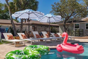A pool area with lounge chairs, umbrellas, and inflatable pool toys. - Palm & Putt Heated Pool Retreat near Anna Maria (Bradenton)