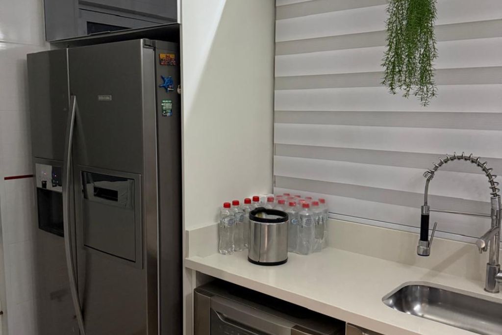 A kitchen with a stainless steel refrigerator, a sink with a modern faucet, and a countertop with water bottles and a thermos.