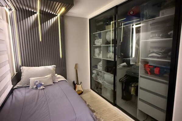 A bedroom with a bed, pillows, a guitar, and a closet with shelves.