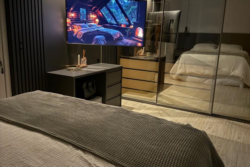 Een moderne hotelkamer met een bed, een bureau met televisie en een kledingkast met spiegel.