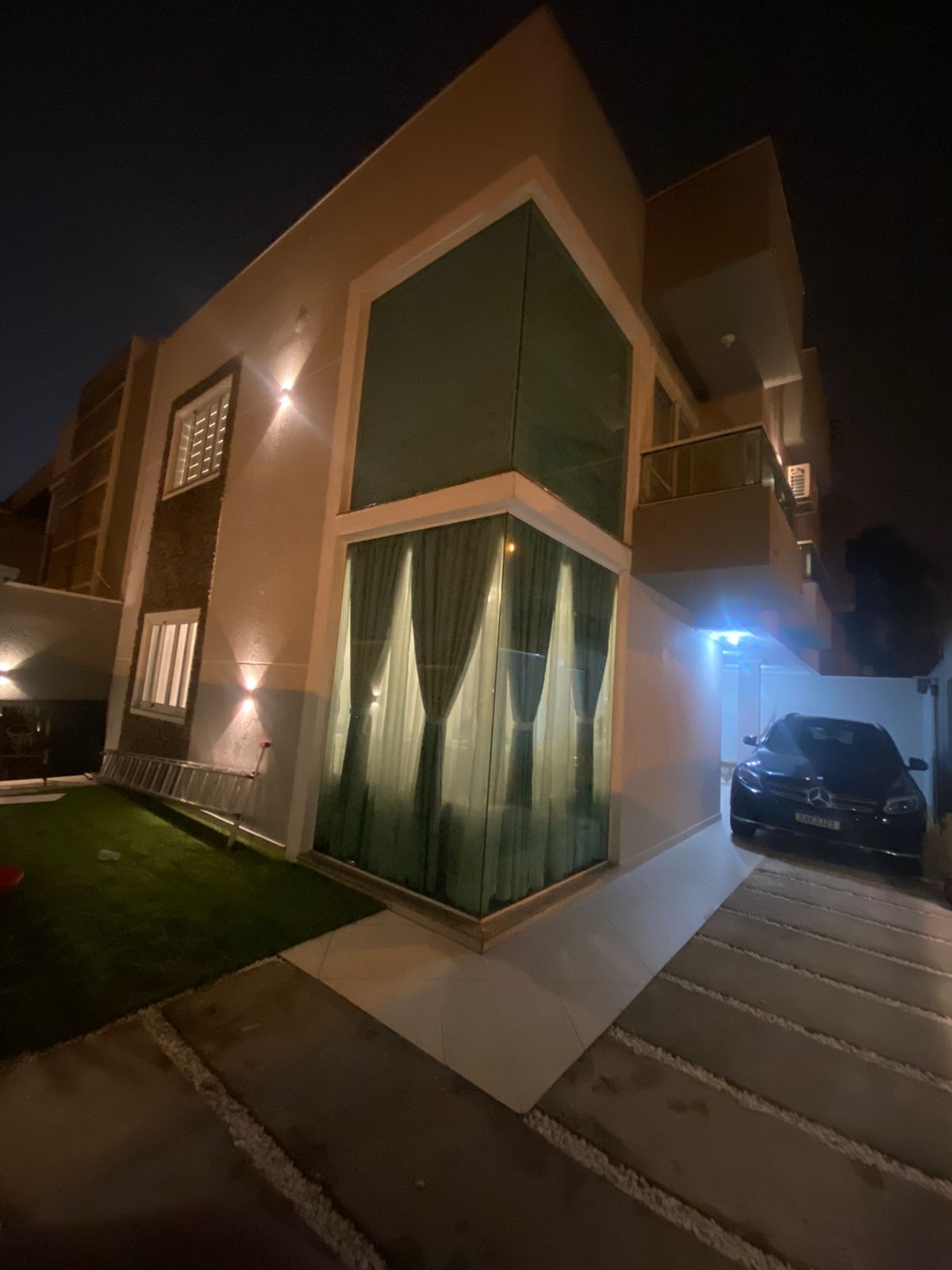 A modern two-story building with a large glass window and a car parked in the driveway.
