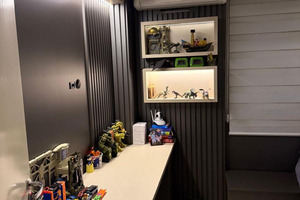 Une pièce avec un bureau, des étagères remplies de jouets et une fenêtre avec des stores.