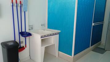 Un baño con lavamanos blanco, cabina de ducha azul y productos de limpieza.