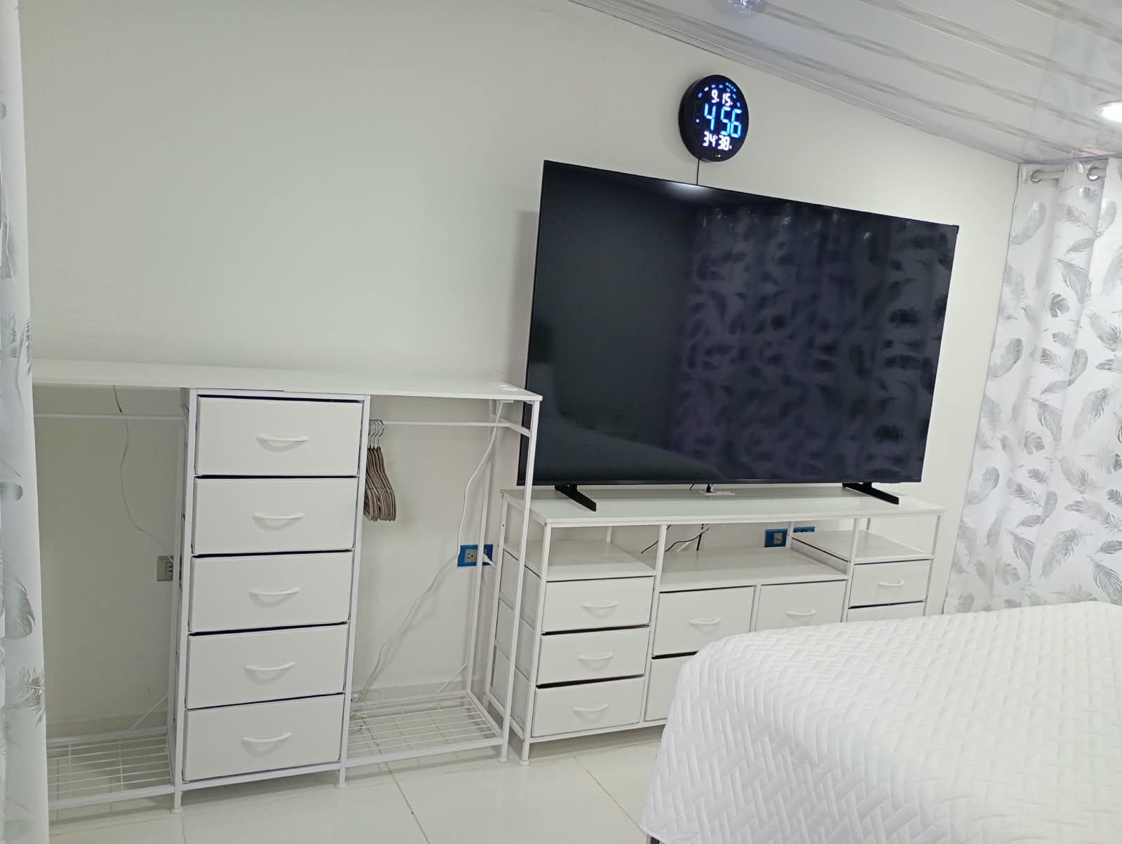 Een slaapkamer met een bed, een tv op een dressoir, een kledingkast en een klok aan de muur.