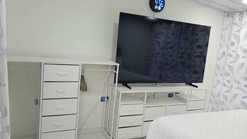 Een slaapkamer met een bed, een tv op een dressoir, een kledingkast en een klok aan de muur.