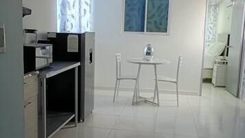 Una cocina limpia y moderna con comedor, pisos de baldosas blancas y un ventanal con cortinas.