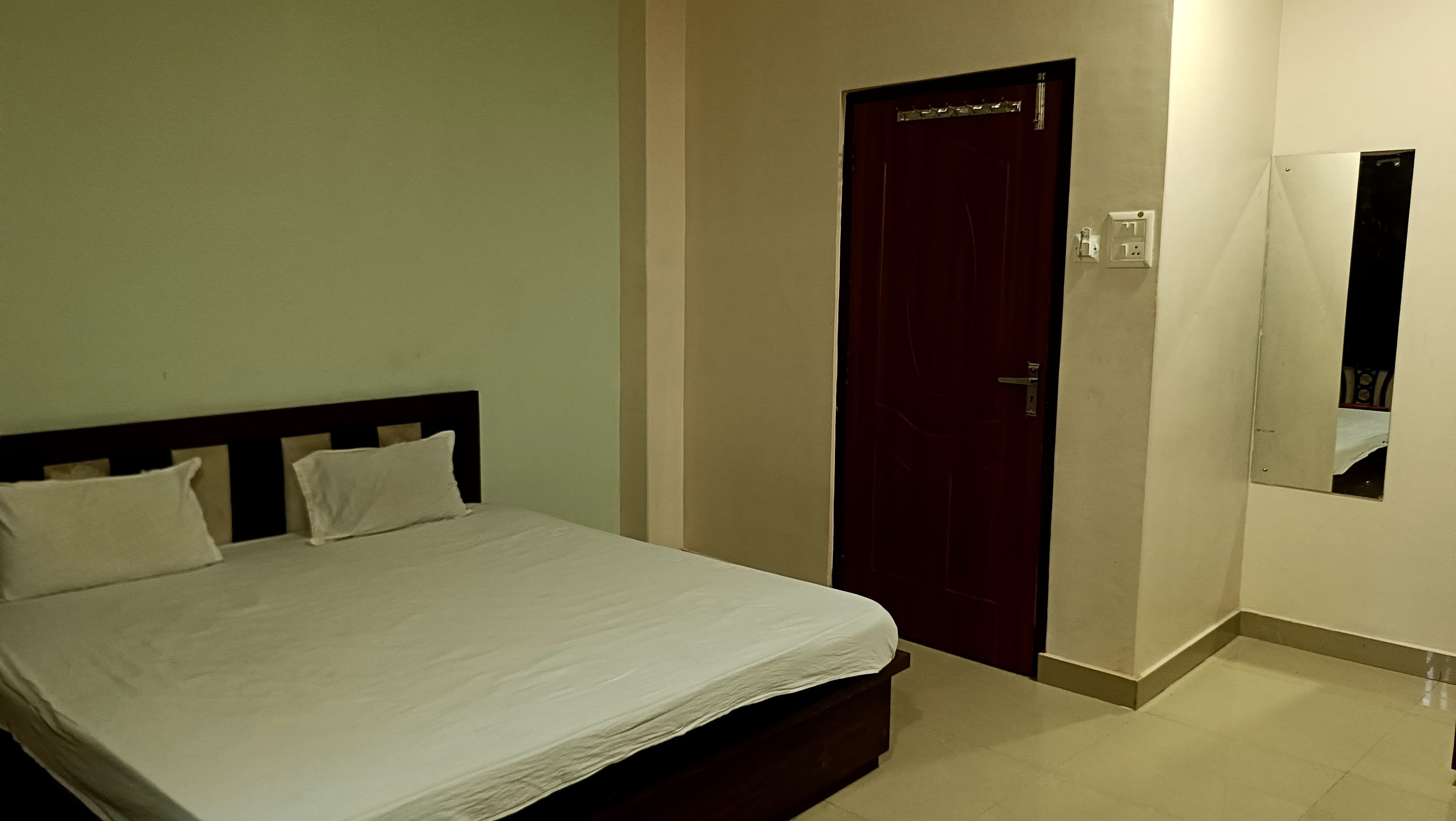 A bedroom with a bed, a door, and a wall-mounted mirror.