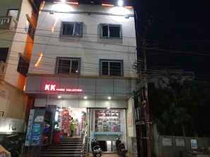 Un edificio de dos pisos con un letrero que dice 'KK Home Solution' en la planta baja. Hay escalones que conducen a la entrada y una motocicleta estacionada afuera.