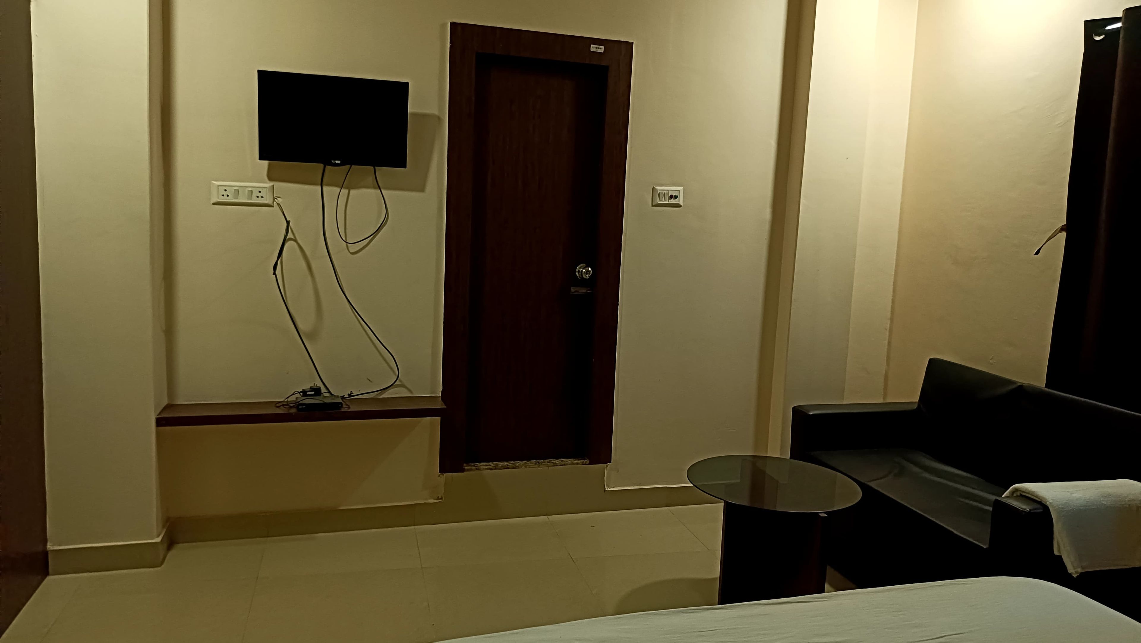 Una habitación de hotel con cama, una mesita, un sofá, un televisor montado en la pared y una puerta.