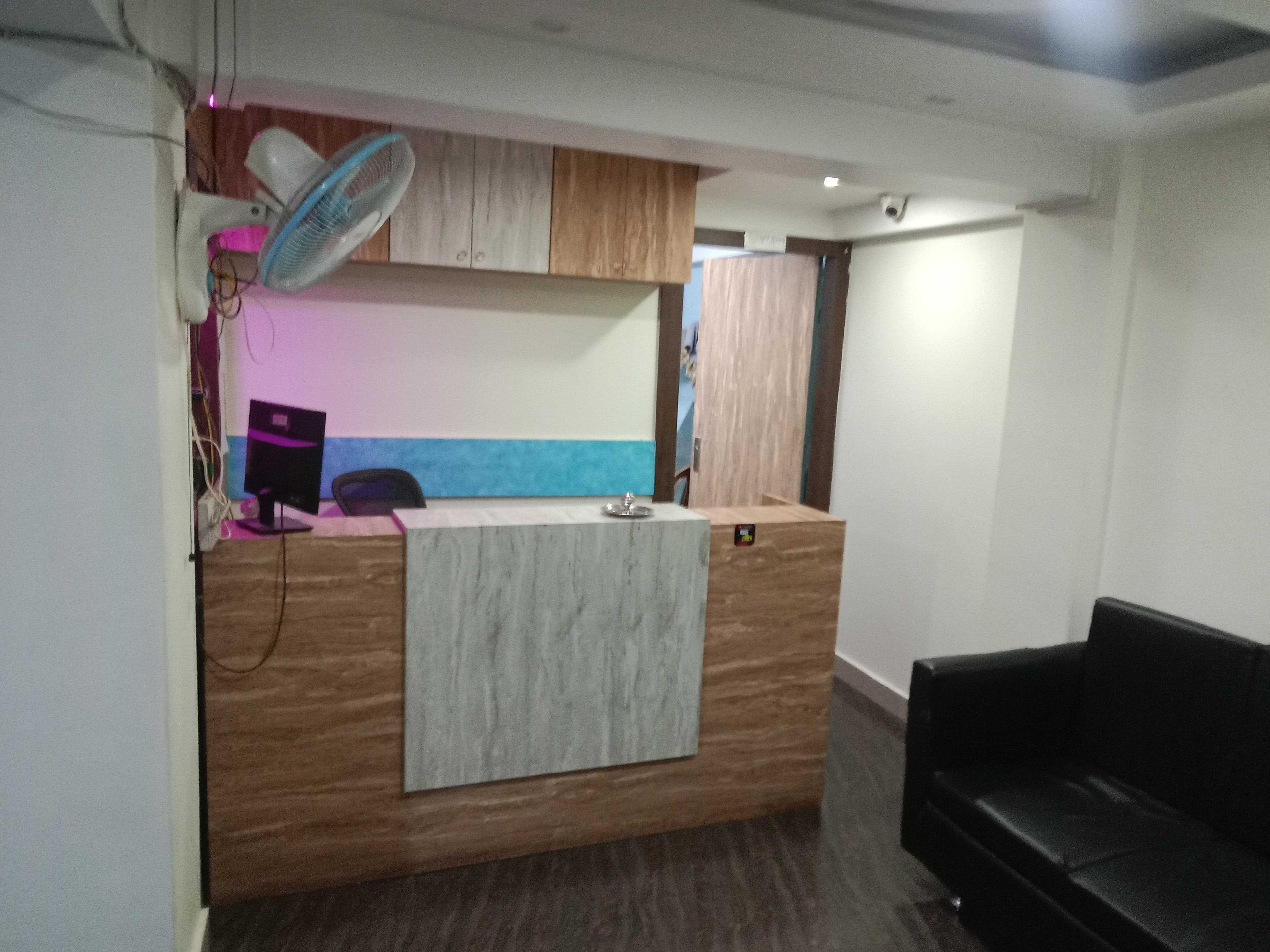 Una recepción con un ventilador, una computadora y una silla. Hay un sofá de cuero negro y un armario de madera.