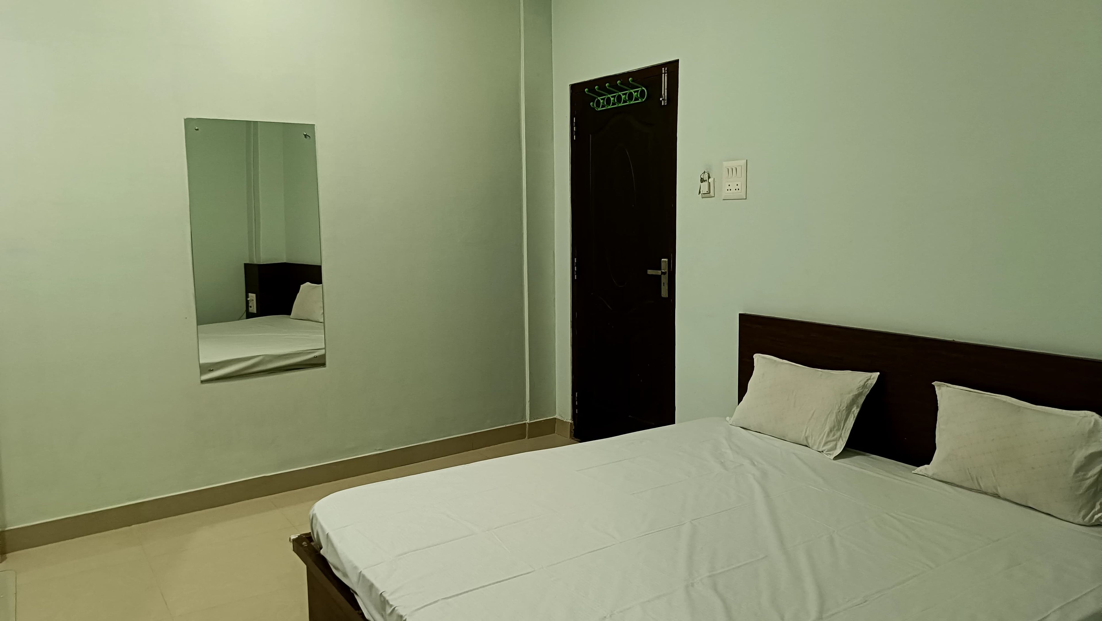 Quarto de hotel com cama, espelho, porta e interruptor de luz.