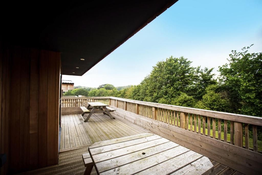 A wooden deck with a picnic table and benches, overlooking a forested area.