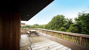 A wooden deck with a picnic table and benches, overlooking a forested area.