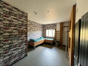 A room with a brick-patterned wall, a single bed with a green bedspread, a window, and a door.