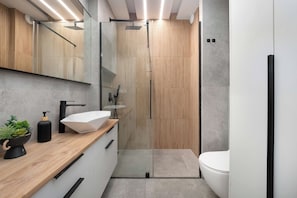 Et moderne badeværelse med en trækommode, en glasbrusekabine og et hvidt toilet.