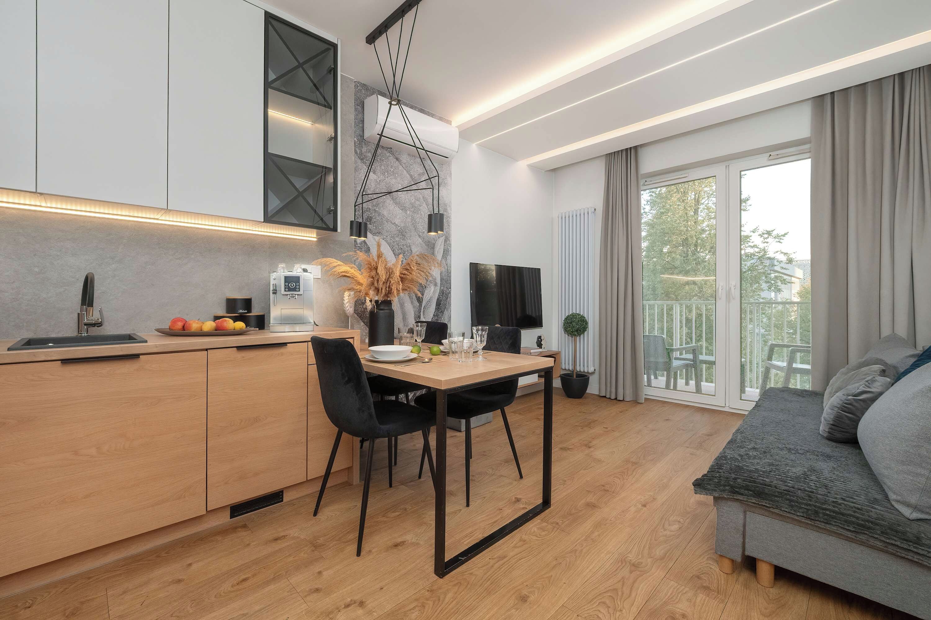 A modern kitchen with a dining area, a flat-screen TV, and a balcony with a view.