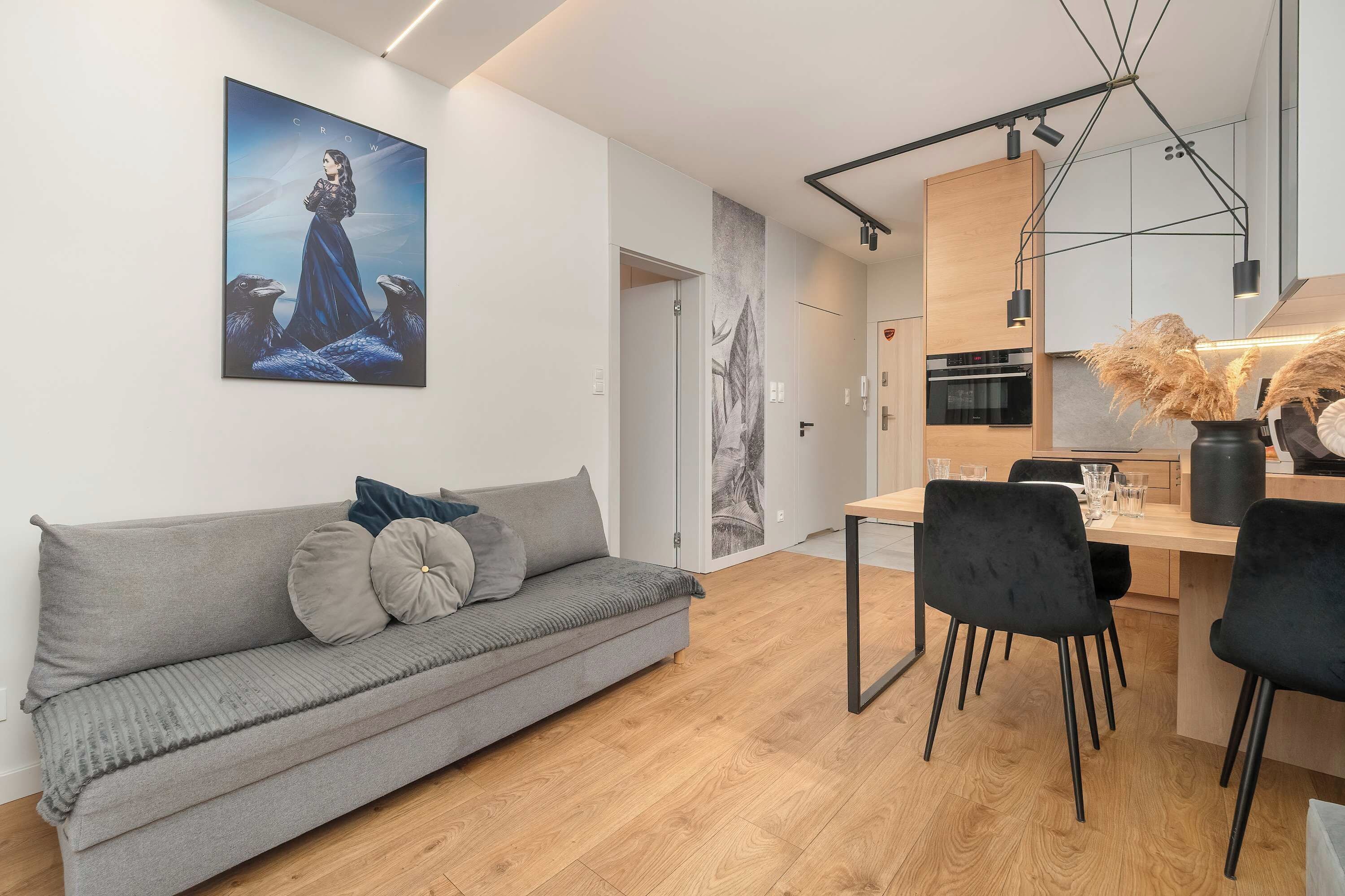 En moderne opholdsstue med en grå sofa, et spiseområde med stole og et køkken med træskabe.