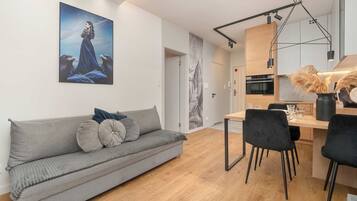 En moderne opholdsstue med en grå sofa, et spiseområde med stole og et køkken med træskabe.