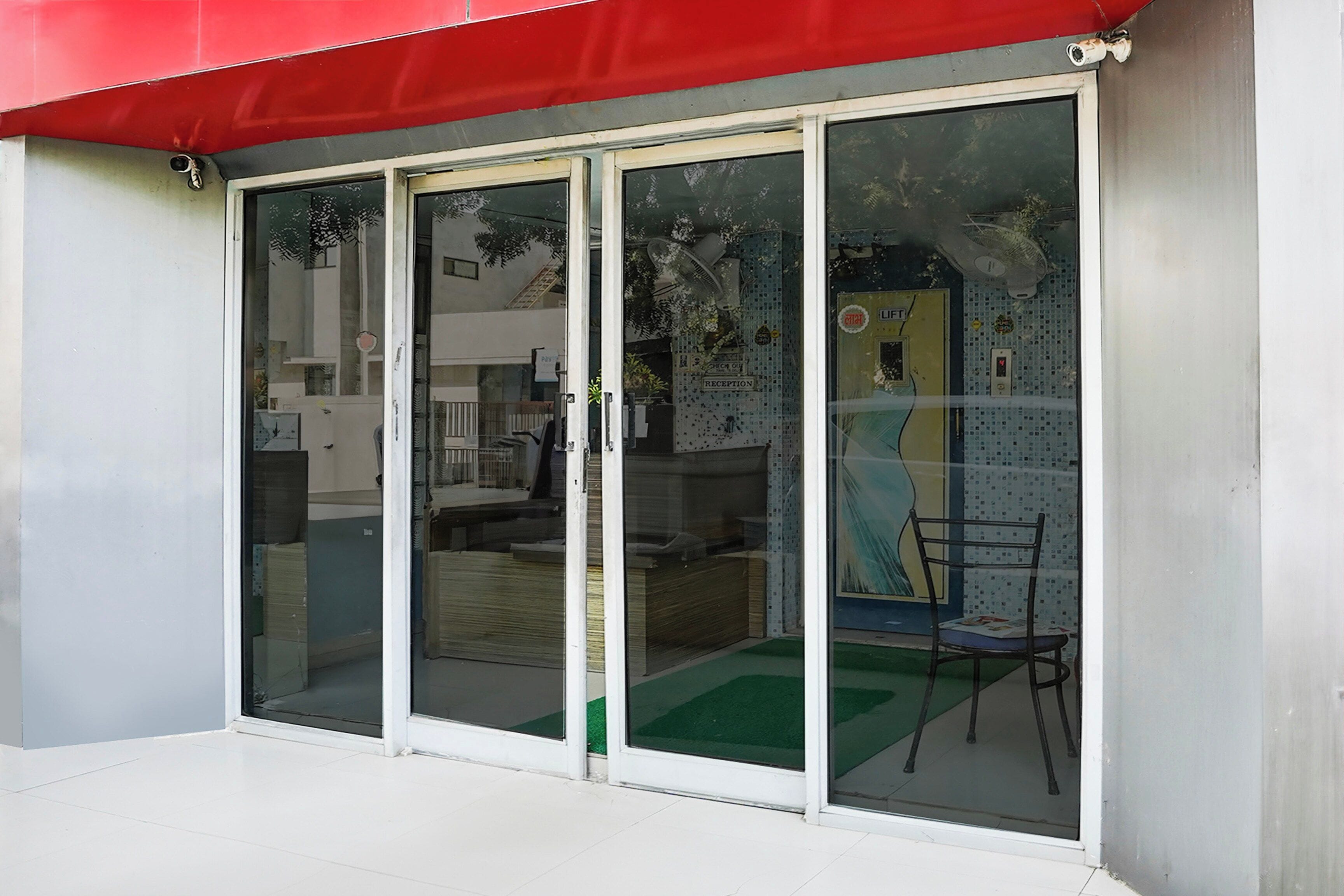 A building entrance with a red awning, a reception area with a chair, and a fan on the wall.