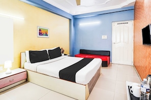 A hotel room with a bed, bedside table, lamp, and a TV mounted on the wall. - Super Hotel O Vibrant Residency (Ahmedabad)