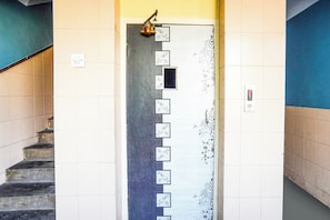 A staircase with a handrail on the left, a wall with a series of framed pictures, and a door with a brass handle. - Super Hotel O Vibrant Residency (Ahmedabad)
