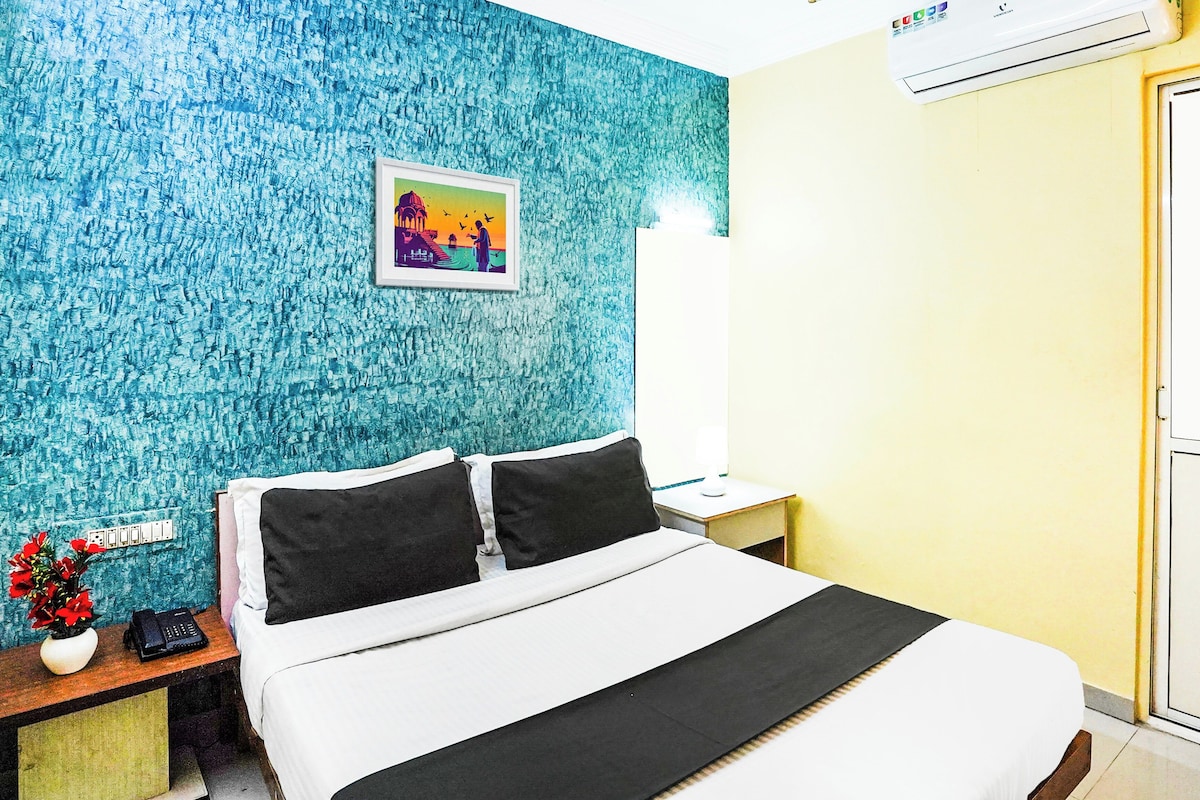 A hotel room with a bed, a nightstand, a lamp, a picture on the wall, and a wall-mounted air conditioner.