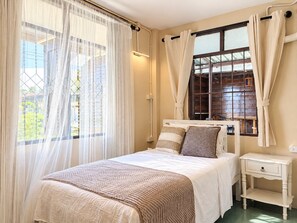 A bedroom with a bed, curtains, a bedside table, and a window. - Tranquil 2-bedroom house with AC in charming Wat Ket Chiang Mai (Chang Wat Chiang Mai)