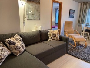 Ein Wohnzimmer mit Sofa, Sessel, Lampe und einem Gemälde an der Wand.