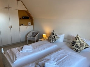 Ein Hotelzimmer mit zwei Betten, einem Sessel, einem Nachttisch mit Lampe und einem Schrank.