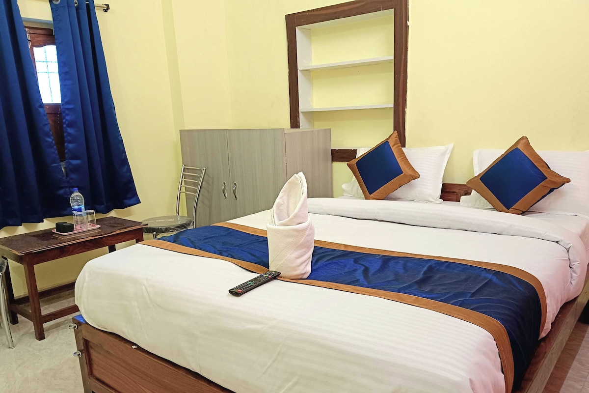 Ein Hotelzimmer mit zwei Betten, einem Holztisch, einem Stuhl, einem Kleiderschrank und einem Fenster mit Vorhängen.