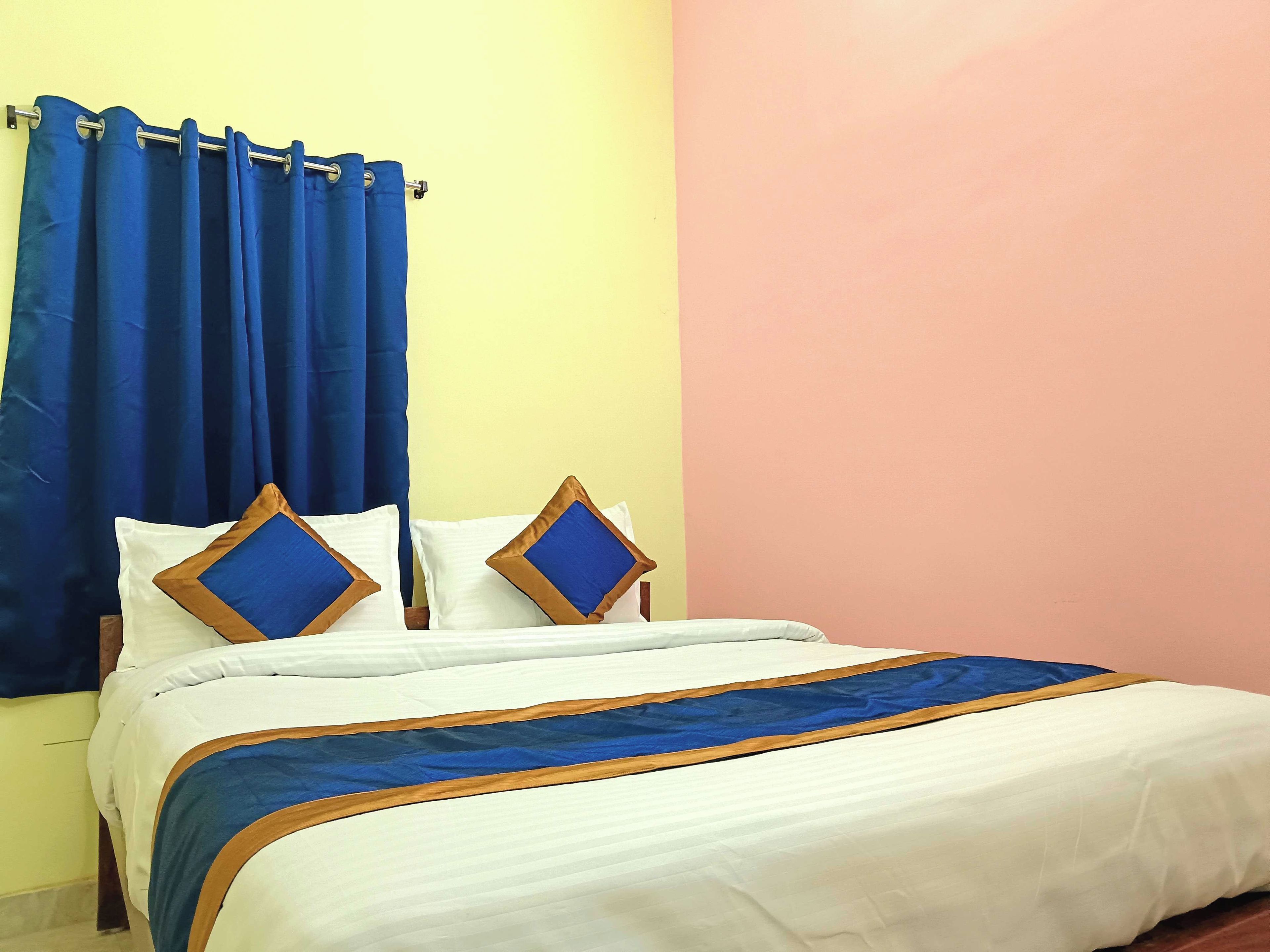 A bed with white bedding and blue accents, a blue curtain, and a pink wall.