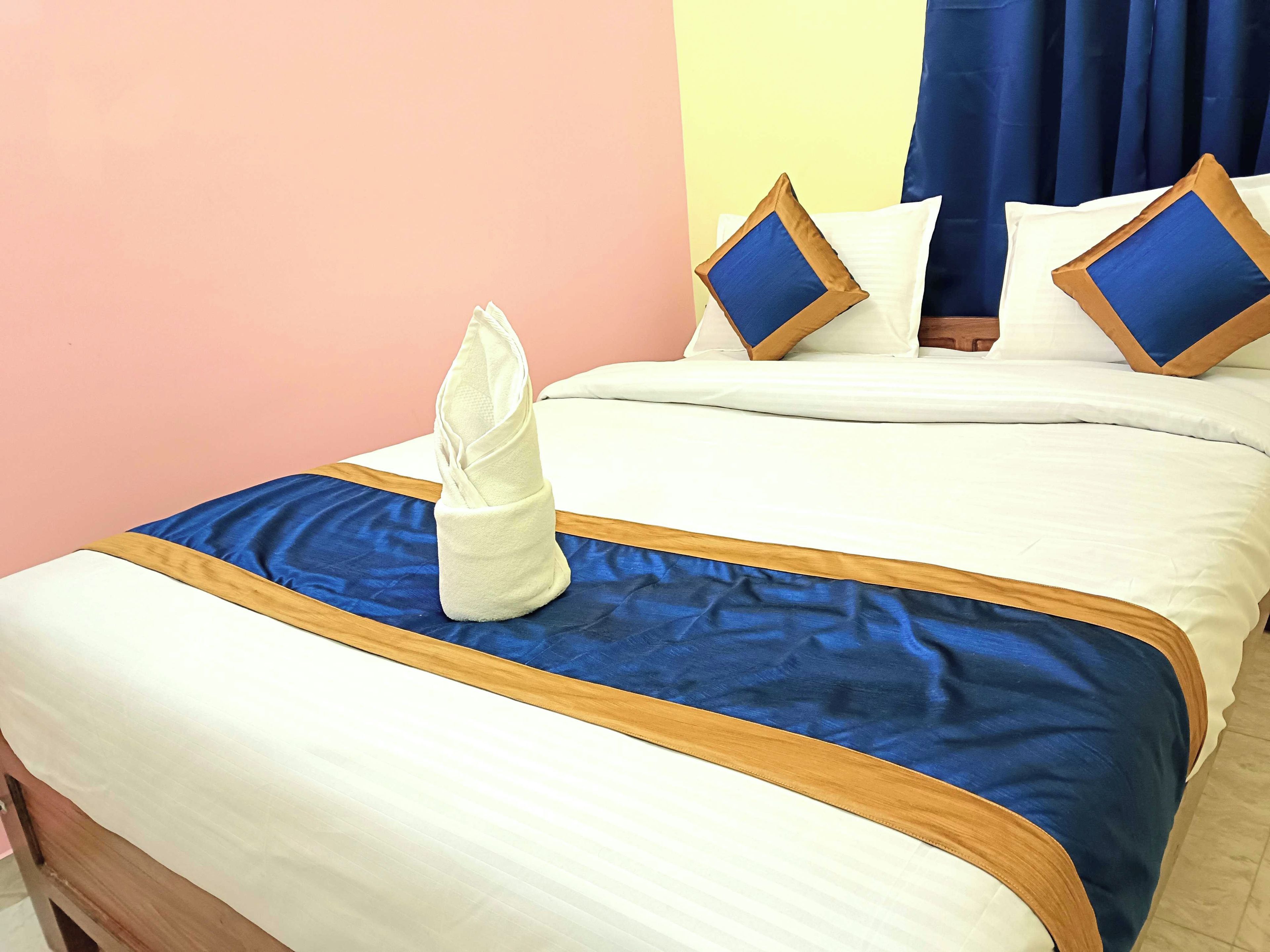 Ein ordentlich bezogenes Bett mit einer blau-weißen Tagesdecke, ein gefaltetes weißes Handtuch und zwei Kissen mit blauen und braunen Akzenten.