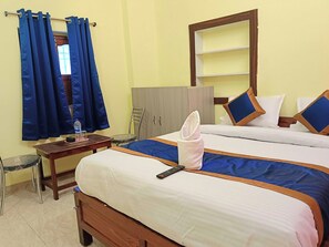 Habitación de hotel con dos camas, cabecera de madera, armario, escritorio con silla y ventana con cortinas.