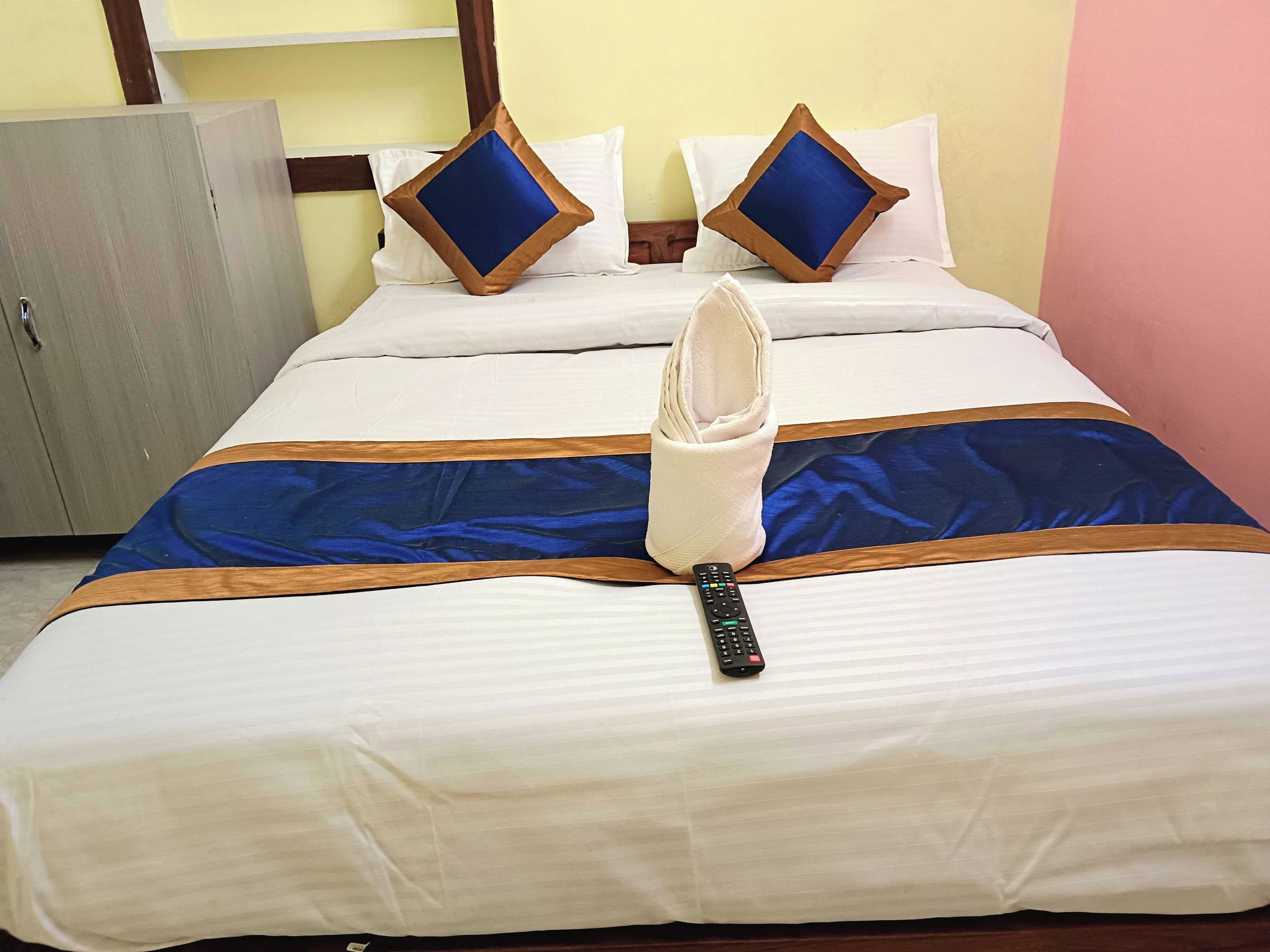 Una cama bien tendida con una colcha azul y marrón, dos almohadas con centros azules, un control remoto y una toalla doblada sobre la cama.