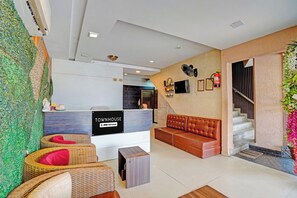 A reception area with a reception desk, a sofa, wicker chairs, a staircase, and a wall with a green leafy design. - Townhouse by OYO Patiala-Zirakpur (Zirakpur)