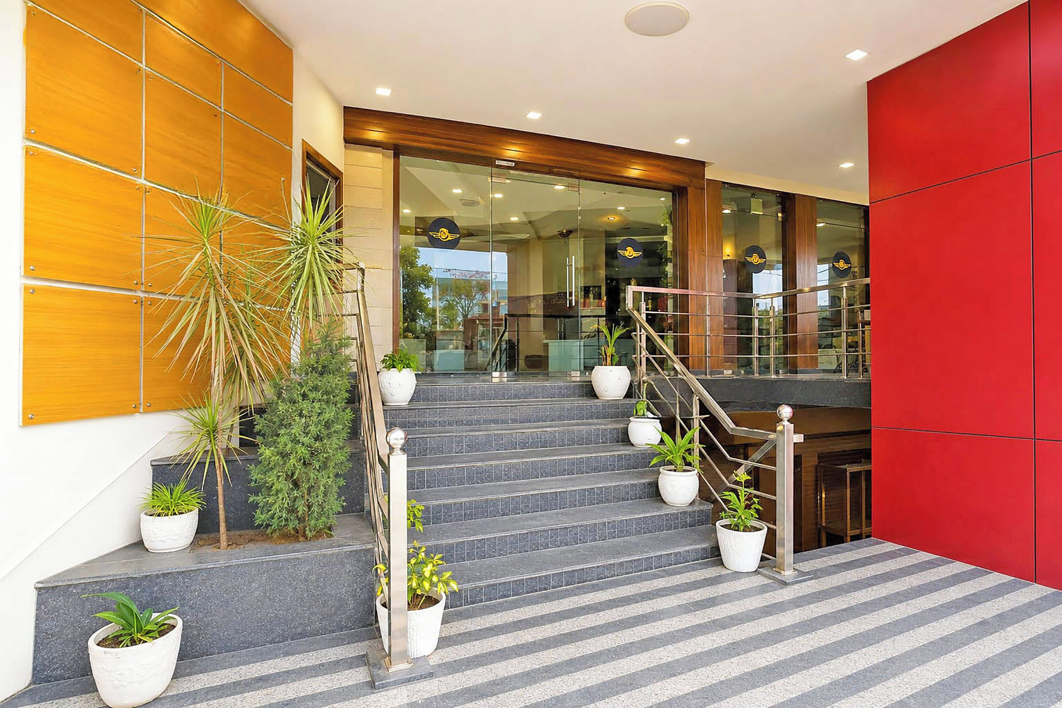Una entrada de hotel moderna con una escalera, plantas en macetas y una pared de acento roja.