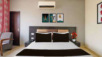 Habitación de hotel con cama, mesitas de noche, una silla, aire acondicionado y una obra de arte en la pared.