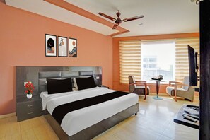 A hotel room with a bed, a desk, a chair, a ceiling fan, and a window with blinds. - Townhouse by OYO Patiala-Zirakpur (Zirakpur)