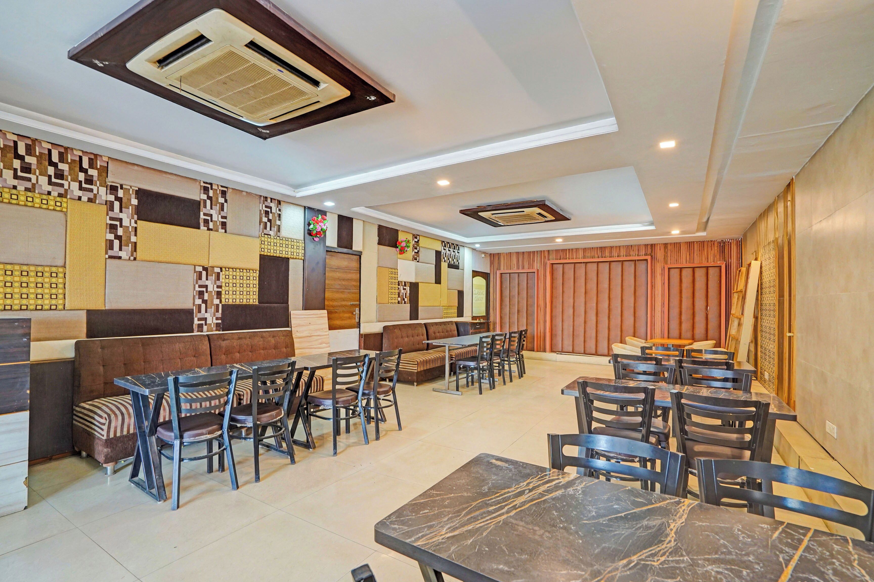 Un restaurante con una decoración moderna, que ofrece diferentes opciones de asientos, como cabinas y mesas, y una pared decorativa con patrones geométricos.