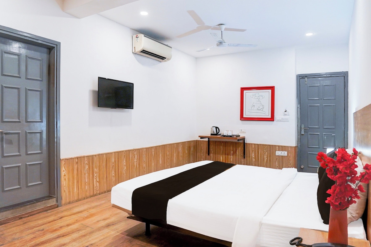 Ein Hotelzimmer mit einem Bett, einem Flachbildfernseher, einer Klimaanlage, einem Deckenventilator, einer Wandverkleidung aus Holz, einem gerahmten Bild und einer Tür.